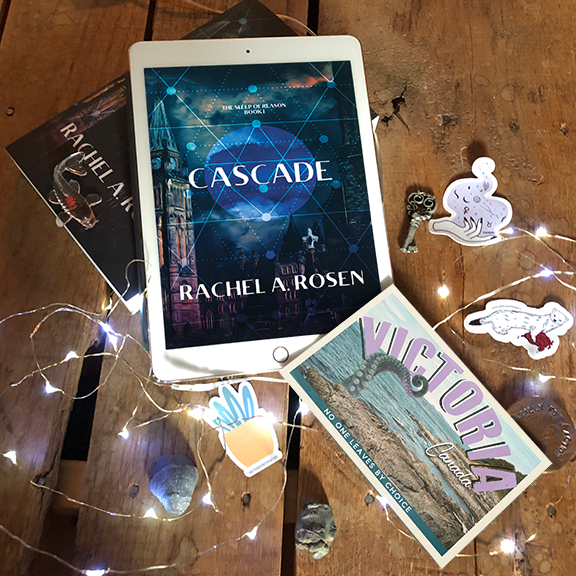 The ebook version of Cascade sitting on the paperback version of Cascade, surrounded by fairy lights and various swag and objects.