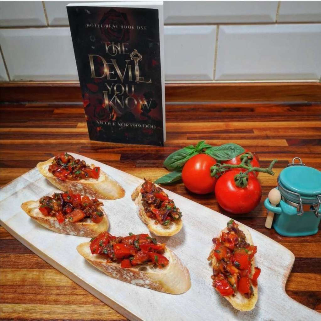bruschetta on a serving tray with fresh tomatoes and Nicole Northwood's "The Devil You Know" in the background