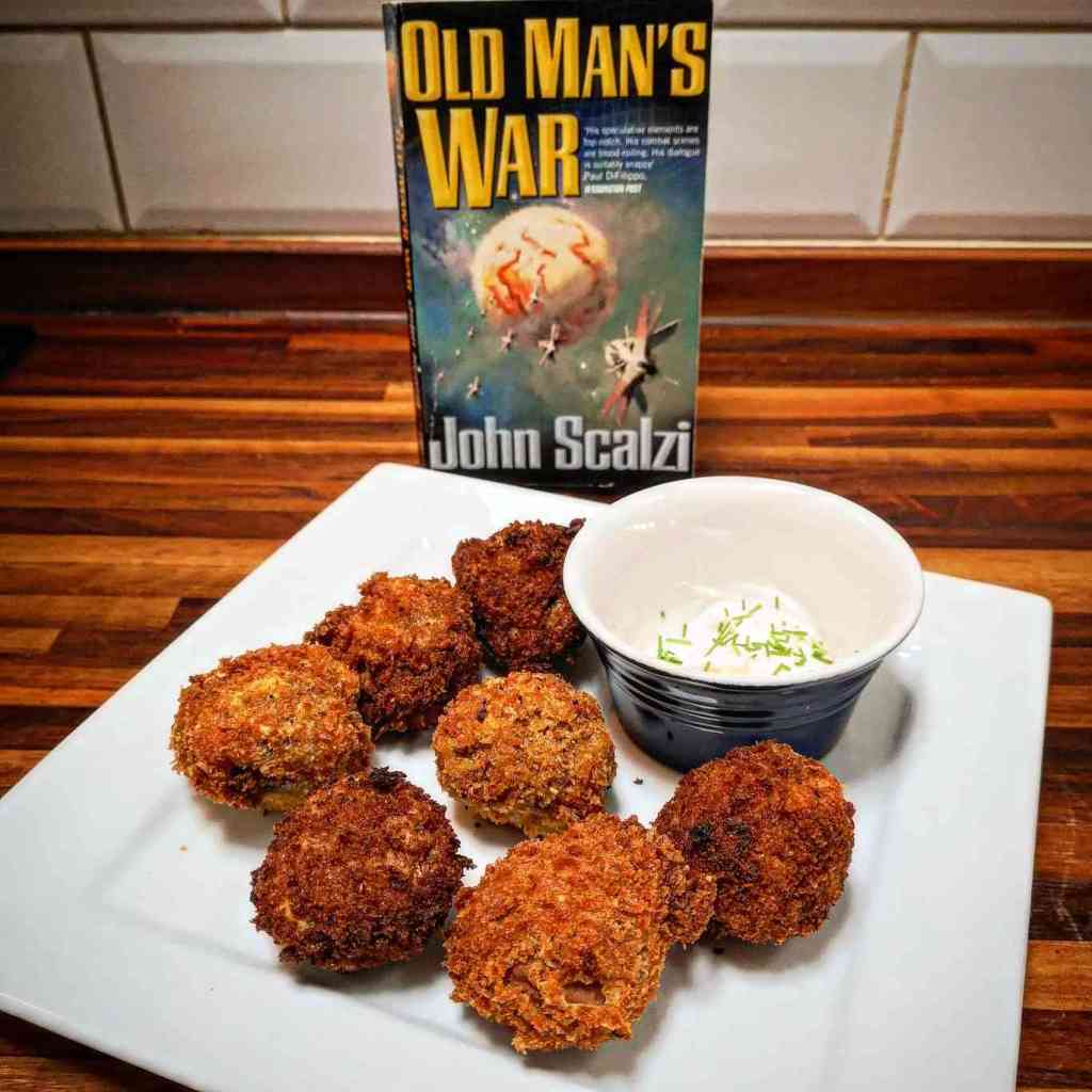 Old Man's War by John Scalzi in front of a plate of breaded mushroom balls with a cup that has some white substance and chives in it.